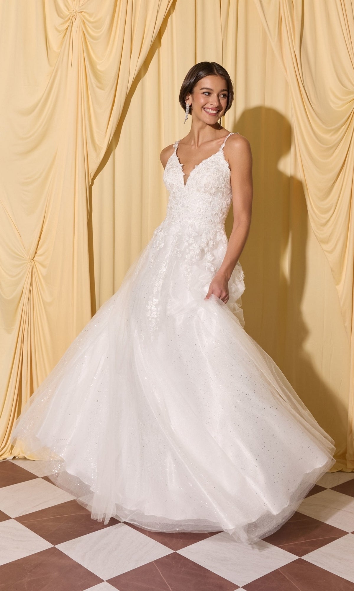 A woman stands on a checkered floor before yellow curtains, smiling in the Long Prom Dress: Eureka EK210 with 3D floral appliques and a full tulle skirt.